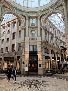 two people are walking in the middle of a shopping mall with an arch above them