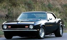 an old black muscle car is parked on the side of the road in front of a hill