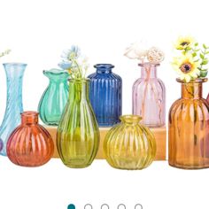 there are many different colored glass vases on the shelf in front of each other