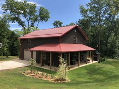 a large brown house with a red roof in the middle of a grassy area next to trees