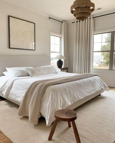 a large white bed sitting in a bedroom next to two windows