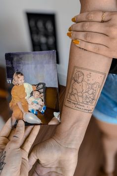 a woman holding up a small child's hand with a tattoo on her arm