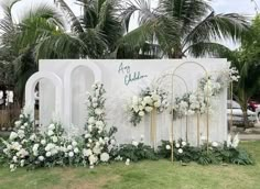 an outdoor wedding setup with white flowers and greenery on the wall, surrounded by palm trees