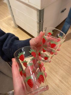 two people are holding glasses with strawberries on the bottom and one has a red strawberry painted on it