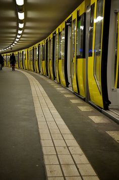 a yellow subway train pulling into a station with people walking by it and onlookers