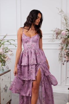 a woman wearing a purple dress with a thigh high slit and floral print on the skirt