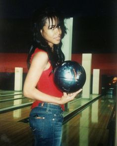 a woman holding a bowling ball in her right hand while standing next to a bowling alley