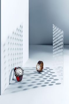 two watches sitting on the floor in front of a white wall with shadows from them