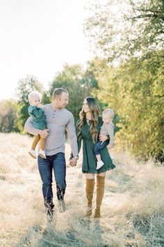 a man and woman walking through tall grass with two babys in their arms while holding hands