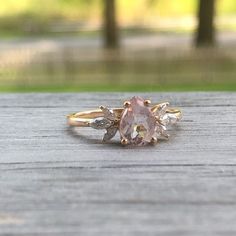 a pink diamond ring sitting on top of a wooden table in front of some trees