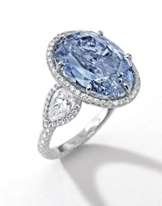 Superb and Rare Fancy Vivid Blue Diamond and Diamond Ring Set with an oval brilliant-cut diamond weighing 10.10 carats, flanked by two pear-shaped diamonds, to the circular-cut diamond surround, gallery and hoop, mounted in 18 karat white gold. Ring size: 6¾ Ice Blue Diamond Ring, Vintage Blue Diamond Ring, Oval Blue Diamond Ring, Light Blue Sapphire Engagement Ring, Blue Diamond Rings, Color Diamond Ring, Blue Diamond Engagement Ring, Expensive Diamond, Blue Diamond Ring