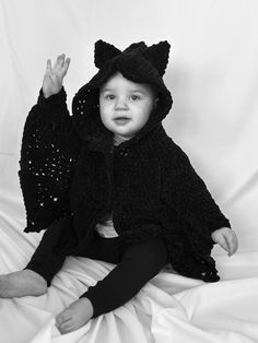 a young child wearing a cat costume on top of a white sheeted bed with her hands in the air