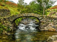 an old stone bridge over a stream in the mountains