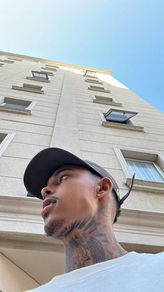 a man with tattoos standing in front of a tall building looking up at the sky