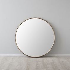 an empty room with a round mirror on the wall and wood flooring in front of it