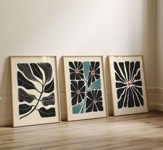 three framed art pieces on the floor in front of a white wall and wood floor