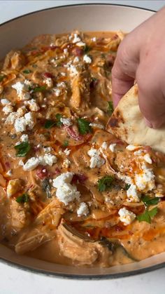 a person dipping some tortilla chips into a bowl full of dip and cheese