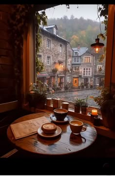 a table with two cups and saucers on it in front of a large window