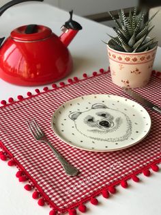 a red and white placemat with a bear face on it next to a potted plant