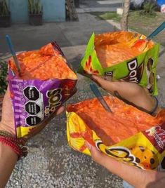 three people holding up two bags of food on the street with chopsticks sticking out of them