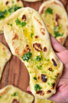 a hand holding up a piece of flat bread with cheese and herbs on it in front of other flat breads