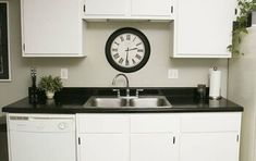 a black and white clock mounted to the wall above a kitchen sink with a dishwasher