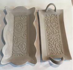 two decorative serving trays with handles on the top one is white and the other is beige