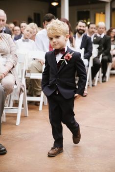 a young boy in a suit and bow tie walking down the aisle at a wedding