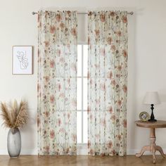 a living room with a large window covered in floral curtains and a vase on the floor