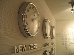 three clocks mounted on the wall above each other in a room with new york written on it