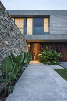 an entrance to a modern house with stone walls and plants in the foreground, at dusk