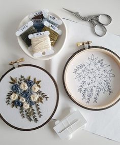 two embroidery hoops with flowers on them next to some scissors and needle holders,