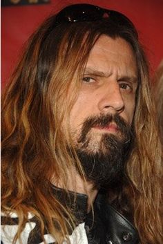 a man with long hair and beard wearing sunglasses looking off to the side while standing in front of a red wall