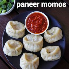 some dumplings are on a black plate with sauce