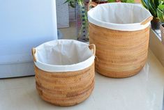 two woven baskets sitting on top of a counter next to potted plants in front of a window