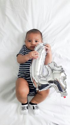 a baby is holding a silver balloon in the shape of a number one on a white sheet