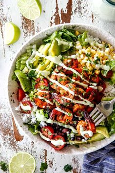 a bowl filled with salad and dressing on top of a table next to limes