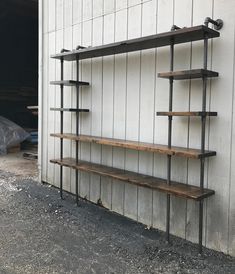 an industrial style shelving unit in front of a white building with metal pipes and wood shelves