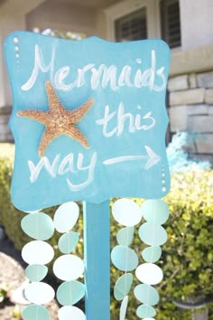 a blue sign that says mermaids this way with a starfish hanging from it