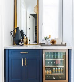 a blue cabinet with a wine cooler in the middle and a mirror above it that has gold trim