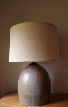 a lamp sitting on top of a wooden table next to a white vase with a beige shade