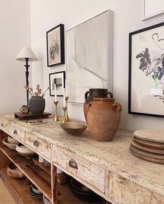 an old wooden table with vases and plates on it in a room filled with framed pictures