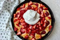 a skillet with strawberries and whipped cream in it on a polka dot cloth