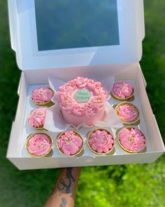 a person is holding a box with cupcakes in it and there are pink frosting on the inside