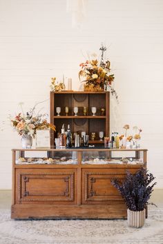 a buffet with flowers and candles on the top is set up in front of a white brick wall