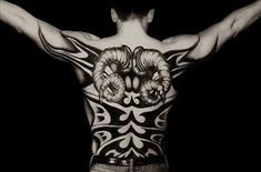 the back of a man's body with tattoos on his chest and arms, in front of a black background