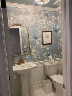 a white toilet sitting next to a sink in a bathroom under a mirror and a light