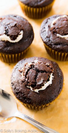 four chocolate cupcakes with white frosting on top and spoon next to them