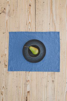 an apple is in a black bowl on a blue napkin next to a wooden table