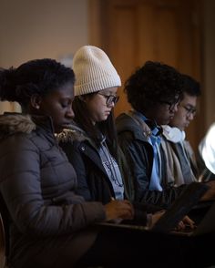 three people are sitting on a bench looking at something in their lap top while wearing winter clothing